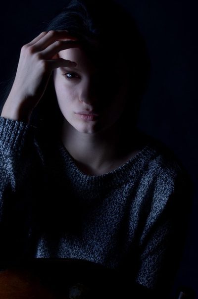 girl in the dark with fingers to her head, staring blankly ahead in thought