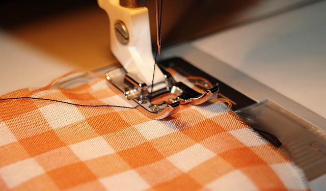 orange and white plaid cloth held under a sewing foot on a sewing machine, ready for sewing